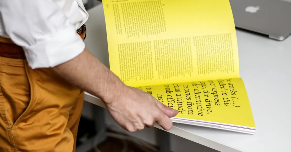 Homme qui feuillette une brochure jaune, avec des colonnes de texte sur les pages