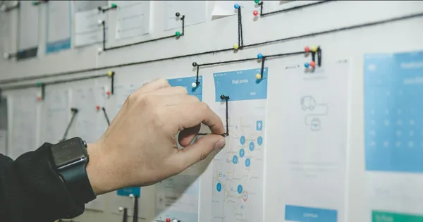 Main qui accroche une fiche sur un tableau de planification couvert de cartes et de post-it