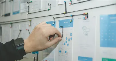Main qui accroche une fiche sur un tableau de planification couvert de cartes et de post-it