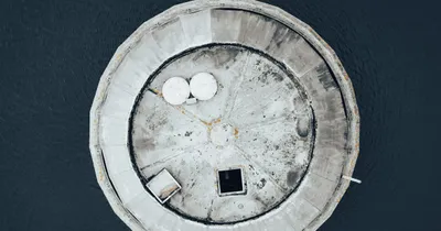 Vue aérienne d'un bassin circulaire de traitement d'eau en béton gris, sur fond sombre