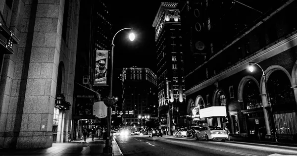Rue de ville nocturne en noir et blanc, réverbère et façades d'immeubles aux arcades sombres