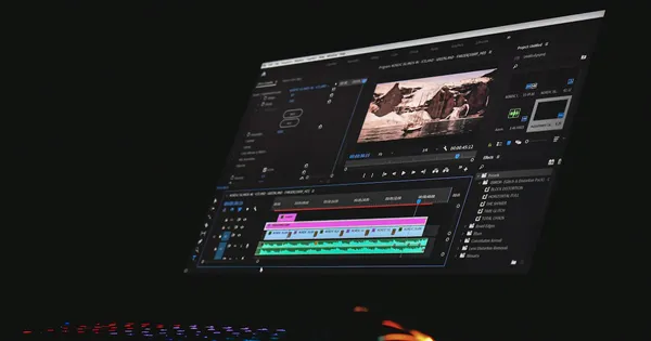 Logiciel de montage vidéo sur écran dans une pièce sombre, avec une timeline et une prévisualisation de paysage