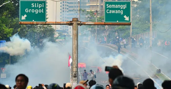 Fumée blanche sur une avenue de Jakarta, avec des manifestants et des panneaux routiers verts au-dessus