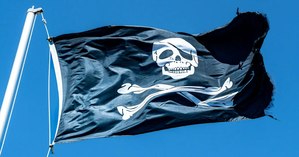 Drapeau pirate noir à tête de mort et tibias croisés, flottant sous un ciel bleu