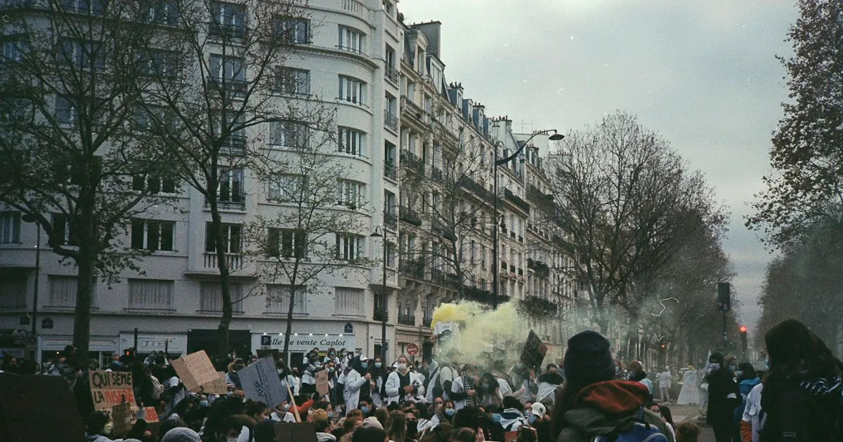 Cortège dans une rue de Paris, bordée d'immeubles haussmanniens, avec des pancartes et une fumée jaune