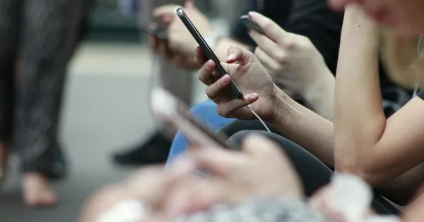 Plusieurs personnes faisant défiler leur téléphone, vues de près, assises côte à côte